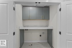 Dedicated laundry alcove featuring bi-fold doors, grey cabinetry with gold-tone hardware, a white countertop with a subtle veined pattern, and coordinating floor tiles - 
