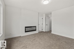Spacious room with a built-in electric fireplace, neutral tone carpeting, and crisp white walls - 