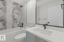 Bathroom featuring a white bathtub, floor-to-ceiling marble-look tile surround, and matte black shower fixtures - 