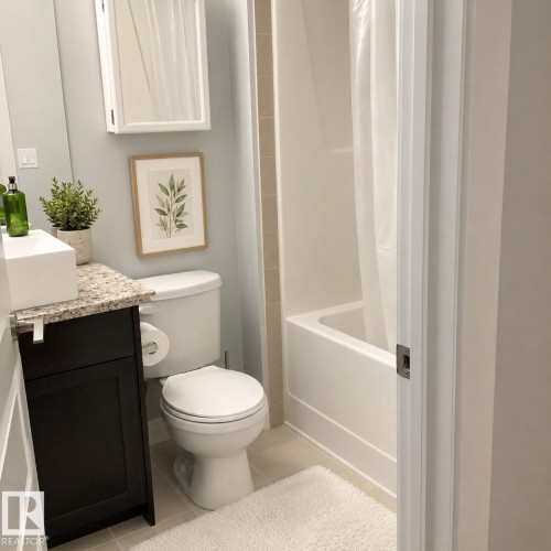Bathroom featuring a dark wood-finish vanity with a light granite countertop, a rectangular vessel sink, a white toilet, and a white bathtub with a shower unit - 531 5151 Windermere Boulevard, Edmonton, AB - Indoor Photo Showing Bathroom