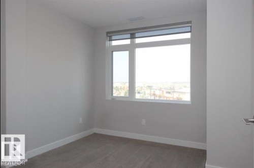 Bright room featuring a large window, neutral wall paint, white baseboards, and gray carpet flooring - 531 5151 Windermere Boulevard, Edmonton, AB - Indoor Photo Showing Other Room