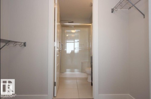 Walk-through closet featuring wire shelving leading into a bathroom with a glass-enclosed shower, white toilet, and dark vanity - 531 5151 Windermere Boulevard, Edmonton, AB - Indoor Photo Showing Bathroom