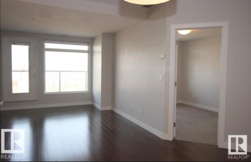 Bright living area featuring wood-finish flooring, a wall of windows, and a glass-paneled door - 531 5151 Windermere Boulevard, Edmonton, AB - Indoor Photo Showing Other Room