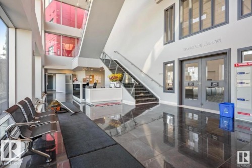 Lobby area featuring high ceilings, dark polished tile flooring, a reception desk, and a multi-level staircase with glass railing - 531 5151 Windermere Boulevard, Edmonton, AB - Indoor Photo Showing Other Room