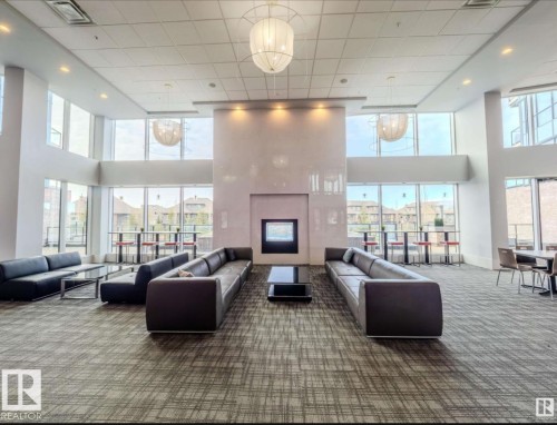 Spacious common area featuring a modern fireplace, high ceilings, large windows, recessed lighting, and patterned carpeting - 531 5151 Windermere Boulevard, Edmonton, AB - Indoor Photo Showing Other Room