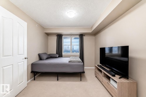 Carpeted room featuring a white paneled door, neutral wall tones, and a window with dark curtains - 404 12025 22 Avenue, Edmonton, AB - Indoor Photo Showing Bedroom