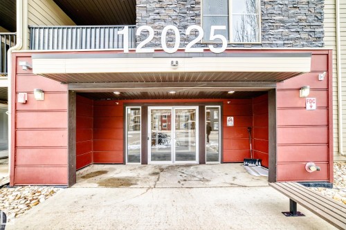 Building entrance featuring red siding, stone facade accents, a sheltered entryway, and glass double doors - 404 12025 22 Avenue, Edmonton, AB - Outdoor With Balcony With Exterior