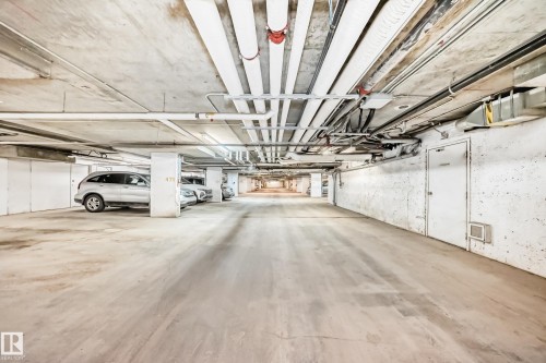Underground parking garage featuring concrete flooring, exposed ceiling utilities, painted concrete walls, and marked parking spaces - 404 12025 22 Avenue, Edmonton, AB - Indoor Photo Showing Garage