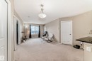 Spacious living area featuring neutral carpeting, a large window with dark drapes, and a decorative ceiling light fixture - 404 12025 22 Avenue, Edmonton, AB  - Indoor Photo Showing Other Room 