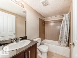 Full bathroom featuring a vanity with an undermount sink, a large mirror with overhead lighting, a toilet, and a bathtub with tile surround - 