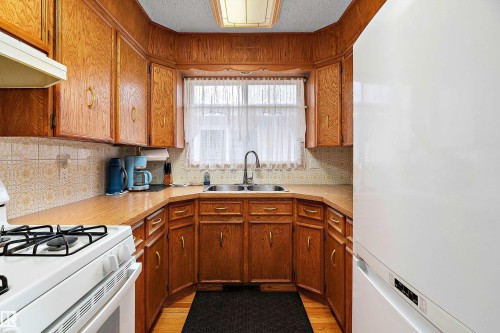 U-shaped kitchen featuring wood cabinetry, laminate countertops, a stainless steel sink with a gooseneck faucet, and a patterned tile backsplash - 15907 101 Street, Edmonton, AB - Indoor Photo Showing Kitchen With Double Sink