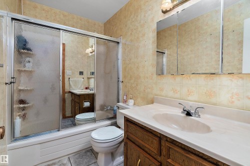 Bathroom featuring a combination tub and shower with sliding glass doors, a vanity with wood-finish cabinetry, an integrated sink, a chrome faucet, and a large mirrored medicine cabinet - 15907 101 Street, Edmonton, AB - Indoor Photo Showing Bathroom
