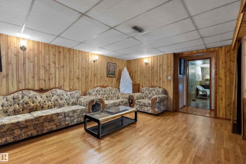 Wood-paneled room with wood-finish flooring, a drop ceiling, and wall-mounted sconce lighting - 15907 101 Street, Edmonton, AB - Indoor