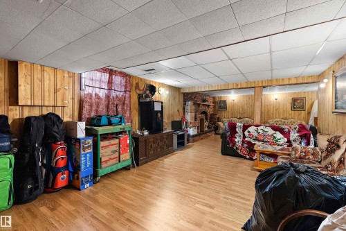 Spacious room featuring wood-finish flooring, wood paneling on walls, a brick fireplace, and ceiling tiles - 15907 101 Street, Edmonton, AB - Indoor