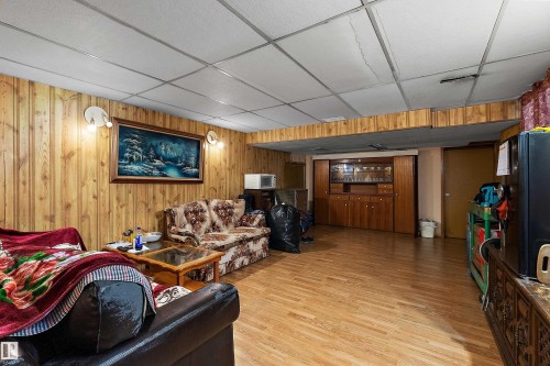 Spacious room featuring wood-finish wall paneling, a grid-patterned ceiling, and wood-finish flooring - 15907 101 Street, Edmonton, AB - Indoor