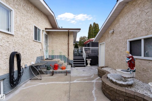 Concrete patio area featuring stucco-finished walls, white-framed windows, and exterior stairs with dark treads and white railings - 15907 101 Street, Edmonton, AB - Outdoor With Exterior