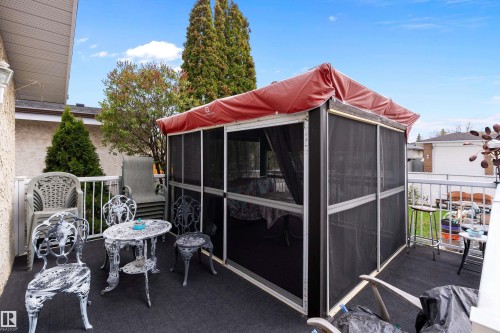 Outdoor deck featuring a screened enclosure with a red canopy, durable outdoor carpeting, white railing, and mature landscaping - 15907 101 Street, Edmonton, AB - Outdoor With Exterior