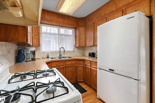 Kitchen featuring wood cabinetry, wood-finish countertops, tile backsplash, and wood-finish flooring - 15907 101 Street, Edmonton, AB - Indoor Photo Showing Kitchen With Double Sink