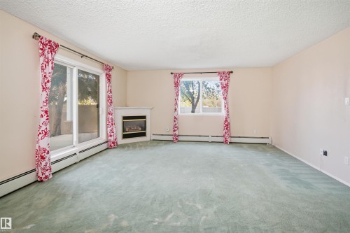 Spacious room featuring light-colored walls, a corner fireplace with a white mantel, and a sliding glass door providing exterior access - 124 10511 42 Avenue, Edmonton, AB 