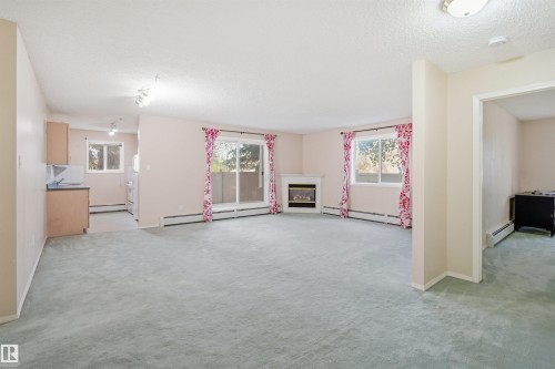 Open concept living area featuring light-colored carpeting, a fireplace with a white mantel, and a sliding glass door - 124 10511 42 Avenue, Edmonton, AB 