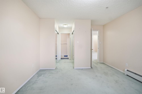 Spacious interior room with light-colored walls and soft green carpeting - 124 10511 42 Avenue, Edmonton, AB 