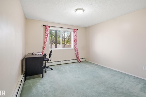 Room featuring soft green carpeting, neutral wall tones, and a window with exterior tree views - 124 10511 42 Avenue, Edmonton, AB 