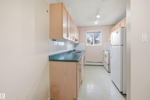 Galley kitchen featuring wood-finish cabinetry, white tile backsplash, and a green countertop - 124 10511 42 Avenue, Edmonton, AB 
