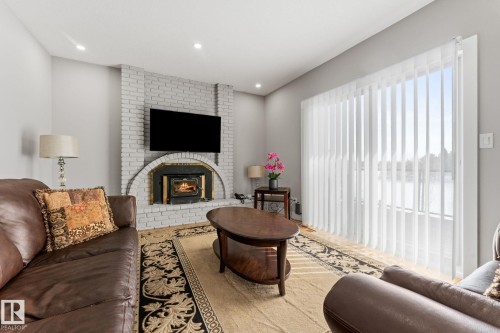 Living area featuring a brick fireplace with an arched hearth, wood-finish flooring, and recessed lighting - 10673 161 Avenue, Edmonton, AB - Indoor Photo Showing Living Room With Fireplace