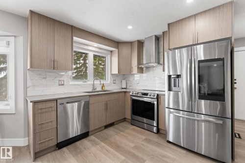 Modern kitchen featuring wood-finish cabinetry, stainless steel appliances, a white marble-patterned backsplash, light-toned countertops, and wood-finish flooring - 10673 161 Avenue, Edmonton, AB - Indoor Photo Showing Kitchen With Upgraded Kitchen