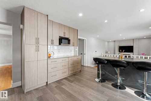 Spacious kitchen featuring extensive cabinetry with modern hardware, a built-in microwave, white tile backsplash, light wood-finish flooring, and recessed ceiling lighting - 10673 161 Avenue, Edmonton, AB - Indoor Photo Showing Kitchen With Upgraded Kitchen