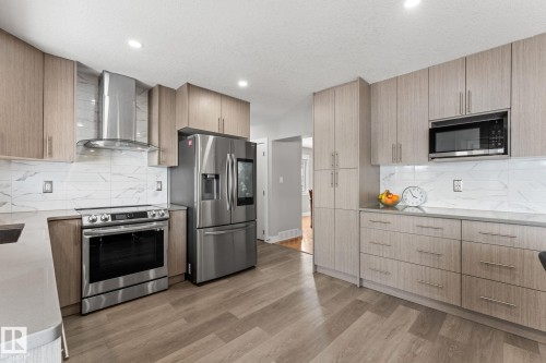 Kitchen featuring wood-finish cabinetry, stainless steel appliances, marble-look tile backsplash, light-toned countertops, and wood-finish flooring - 10673 161 Avenue, Edmonton, AB - Indoor Photo Showing Kitchen With Upgraded Kitchen
