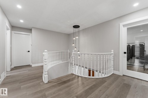 Curved staircase with white balusters, wood-finish flooring, recessed lighting, and a modern tiered pendant light fixture - 10673 161 Avenue, Edmonton, AB - Indoor Photo Showing Other Room