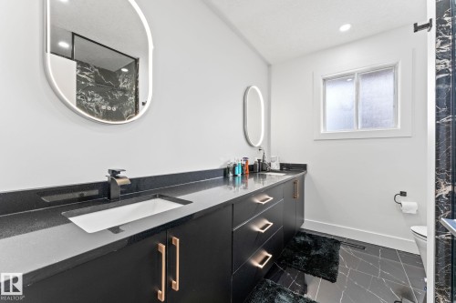 Modern bathroom featuring a dual vanity with black cabinetry and golden hardware, sleek black countertops, and under-mount sinks - 10673 161 Avenue, Edmonton, AB - Indoor Photo Showing Bathroom