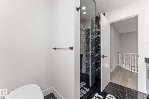 Bathroom featuring a glass-enclosed shower with black marble-finish tile, black marble-finish floor tile, a sleek white toilet, and matte black fixtures - 10673 161 Avenue, Edmonton, AB - Indoor