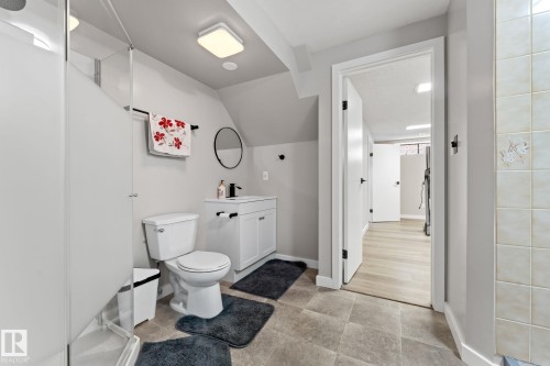 Bathroom featuring square floor tiles, a white vanity with integrated sink, a circular wall mirror, and a frosted glass shower enclosure - 10673 161 Avenue, Edmonton, AB - Indoor Photo Showing Bathroom