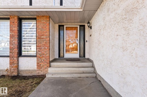 Entryway featuring a clear glass door with white framing, concrete steps, a black sconce, and brick-column accents - 10673 161 Avenue, Edmonton, AB - Outdoor