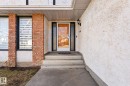 Entryway featuring a clear glass door with white framing, concrete steps, a black sconce, and brick-column accents - 10673 161 Avenue, Edmonton, AB  - Outdoor 