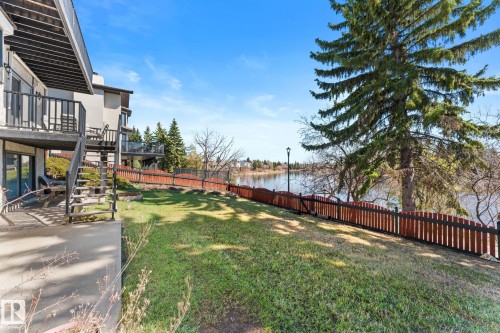 Expansive green space featuring a wood fence, mature evergreen tree, and water frontage - 10673 161 Avenue, Edmonton, AB - Outdoor With Balcony