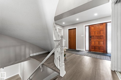 Curved staircase with white railing, wood-finish flooring, recessed lighting, and a paneled wood entry door with frosted sidelights - 10673 161 Avenue, Edmonton, AB - Indoor Photo Showing Other Room