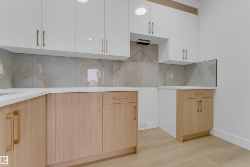 Modern kitchen featuring two-tone cabinetry with white upper cabinets and wood-finish lower cabinets, light-toned countertops, and a full tile backsplash - 449 Crystal Creek Link, Leduc, AB - Indoor Photo Showing Kitchen