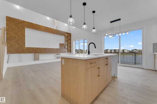Spacious interior featuring light wood-finish flooring, a kitchen island with a white countertop and black gooseneck faucet, and a large sliding glass door opening to a balcony - 449 Crystal Creek Link, Leduc, AB - Indoor Photo Showing Kitchen