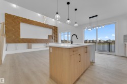 Spacious interior featuring light wood-finish flooring, a kitchen island with a white countertop and black gooseneck faucet, and a large sliding glass door opening to a balcony - 