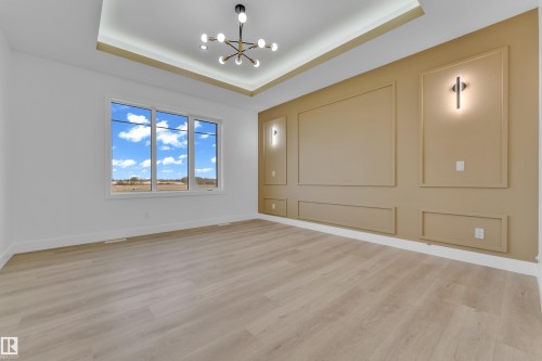 Spacious room featuring light wood-finish flooring, a contemporary chandelier, and a tray ceiling with integrated lighting - 449 Crystal Creek Link, Leduc, AB - Indoor Photo Showing Other Room