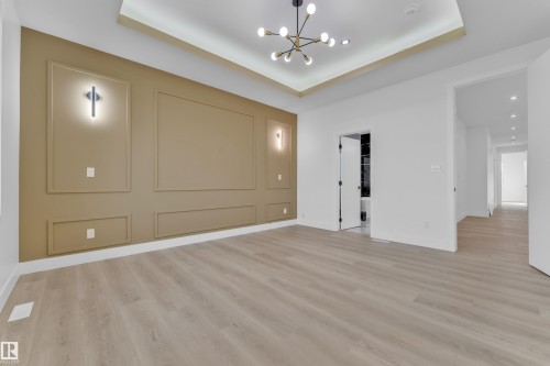 Spacious room featuring light wood-finish flooring, a tray ceiling with recessed lighting and a modern chandelier, and a decorative accent wall with wall sconces - 449 Crystal Creek Link, Leduc, AB - Indoor Photo Showing Other Room