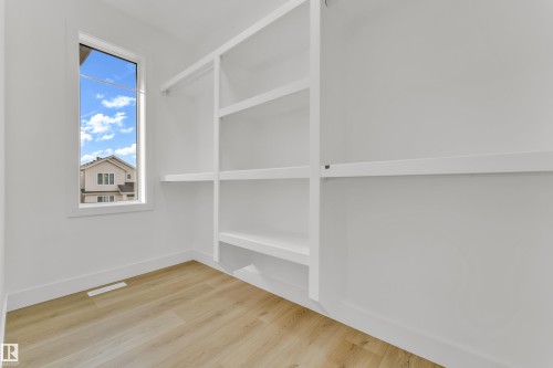 Walk-in closet featuring built-in shelving, hanging rods, wood-finish flooring, and a vertical window - 449 Crystal Creek Link, Leduc, AB - Indoor Photo Showing Other Room