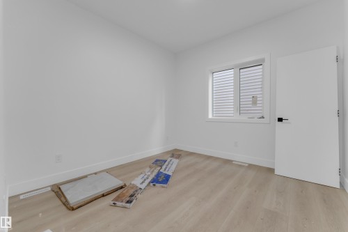 Bright room featuring a large window with white blinds, light wood-finish flooring, white baseboards, and a modern white door with black hardware - 449 Crystal Creek Link, Leduc, AB - Indoor Photo Showing Other Room
