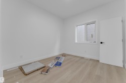 Bright room featuring a large window with white blinds, light wood-finish flooring, white baseboards, and a modern white door with black hardware - 