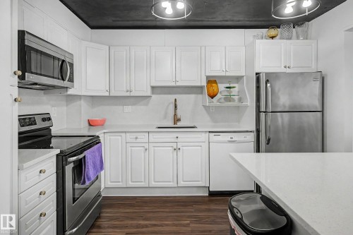 Modern kitchen featuring white cabinetry, stainless steel appliances, light-toned countertops, and wood-finish flooring - 1205 10045 118 Street, Edmonton, AB - Indoor Photo Showing Kitchen