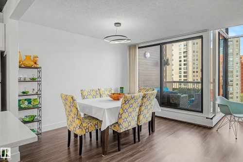 Bright dining area featuring wood-finish flooring, a contemporary circular pendant light, and a full-height glass sliding door opening to a private balcony - 1205 10045 118 Street, Edmonton, AB - Indoor Photo Showing Dining Room