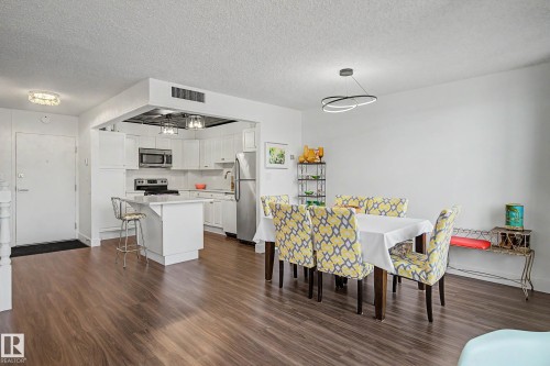 Open-concept living space featuring wood-finish flooring, a contemporary ceiling light fixture, and a kitchen with white cabinetry - 1205 10045 118 Street, Edmonton, AB - Indoor Photo Showing Other Room